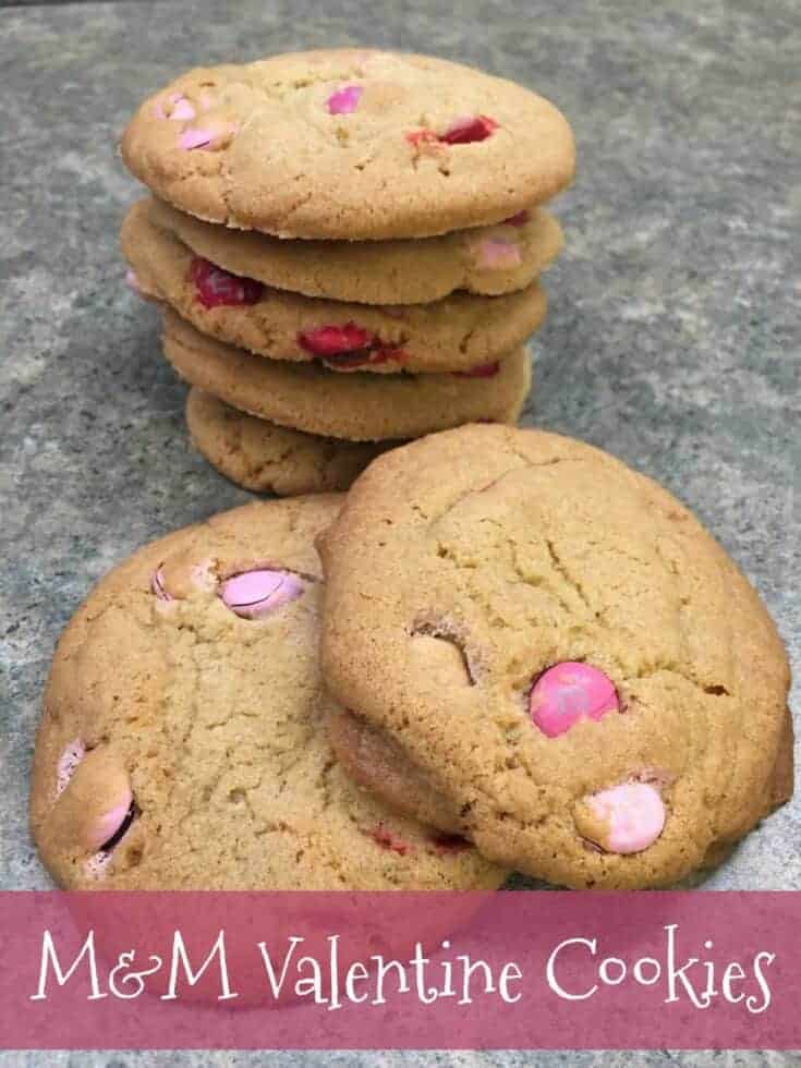 Pink and white M&M cookies stacked on a counter