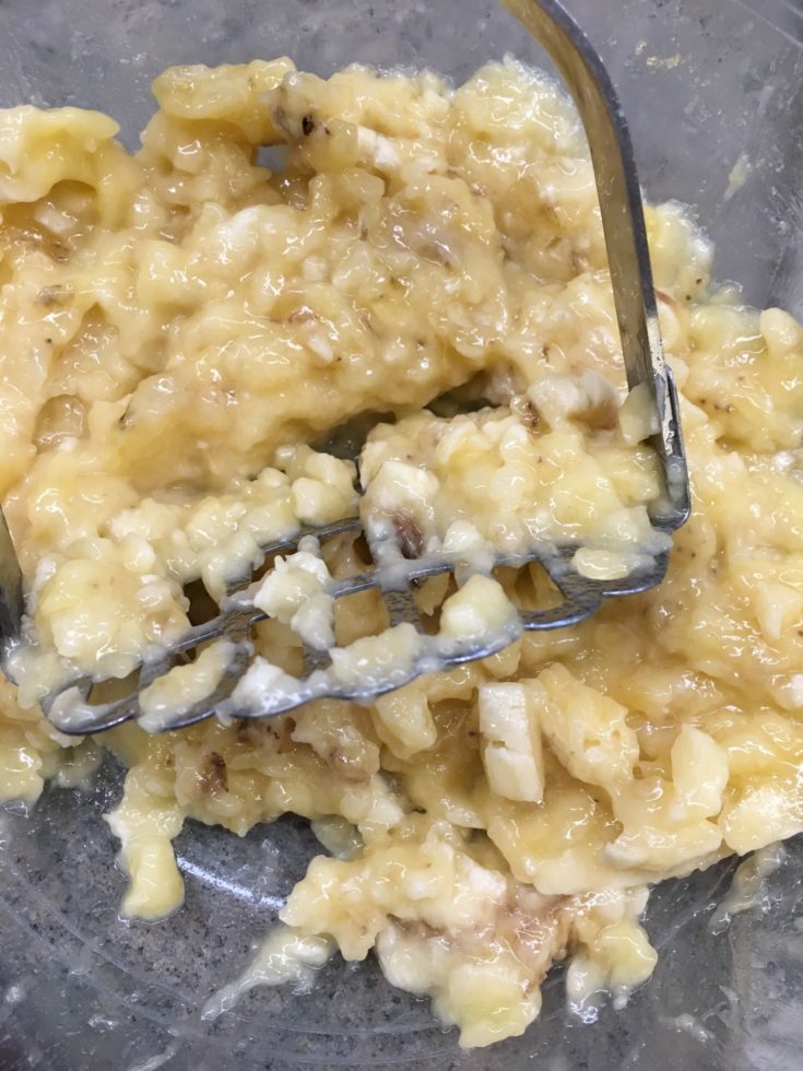 Bananas being mashed with a potato masher in a bowl