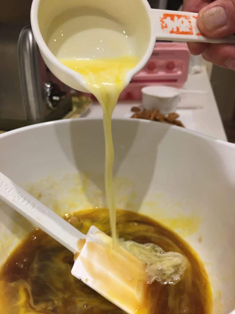 Pouring melted butter into the bowl of pecan pie ingredients