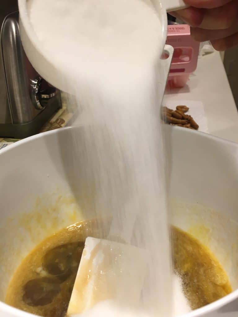 Pouring sugar into the bowl of pecan pie ingredients