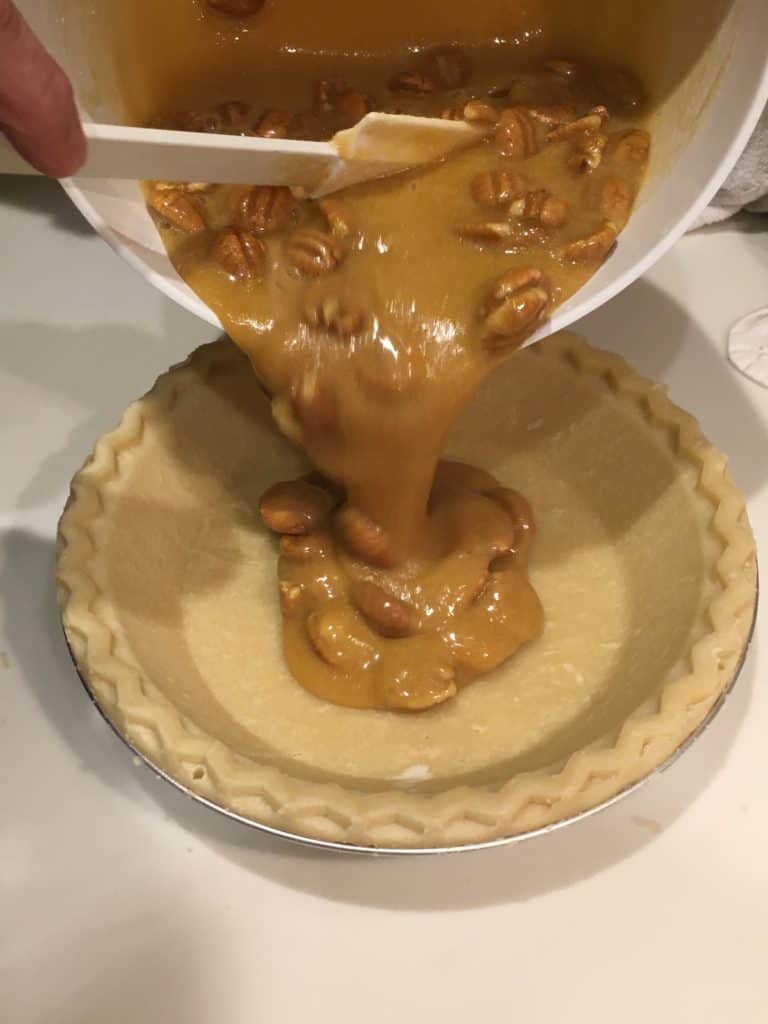 Pouring pecan pie ingredients into a pie crust.