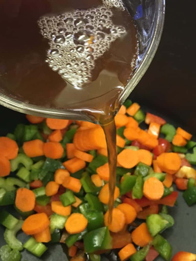 Pouring beef broth into a saucepan with vegetables for hamburger potato soup