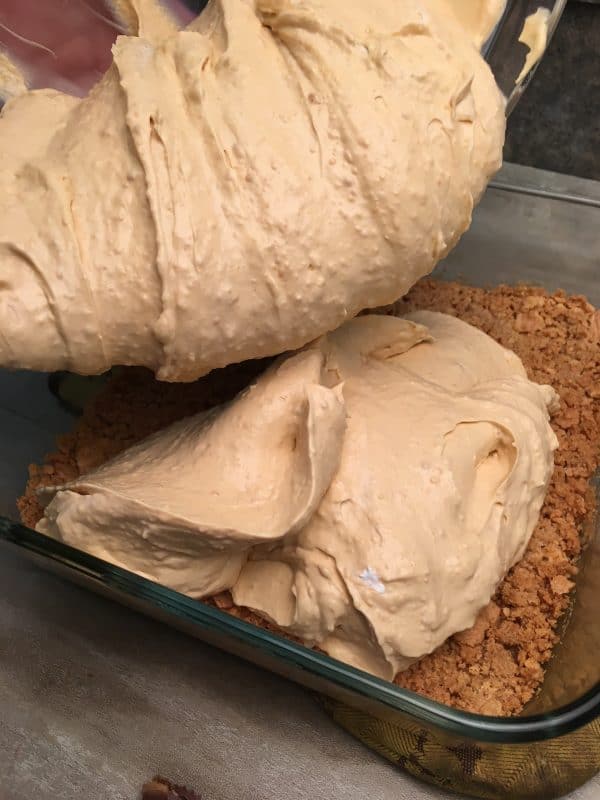 Peanut butter chocolate dessert being poured into a small square casserole dish