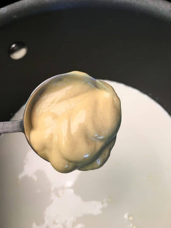 Dijon mustard on a measuring spoon over the saucepan