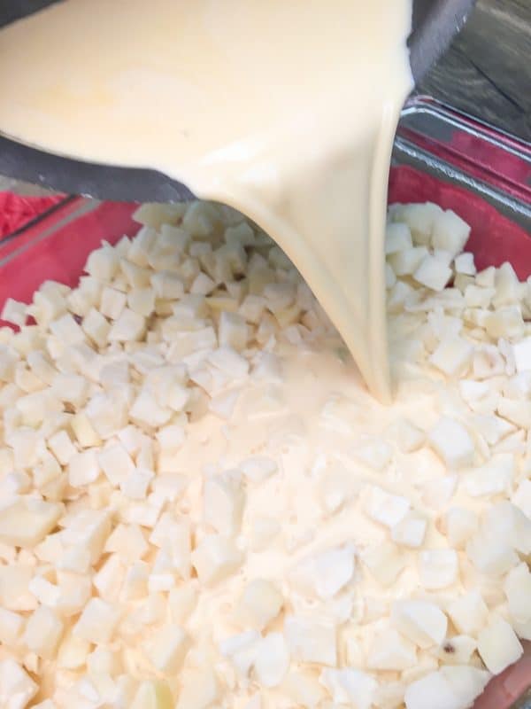 Pouring melted cheese and heavy cream into a casserole dish on top of diced potatoes