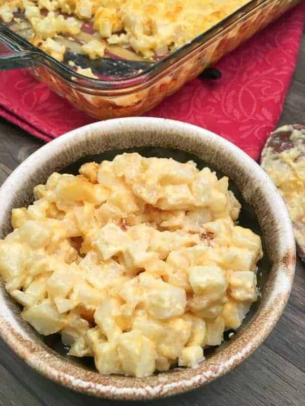 Cheesy diced potatoes in a bowl next to a casserole dish. 