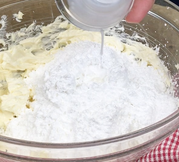 Picture of powdered sugar, cream cheese, and butter mixed together in a glass bowl. 