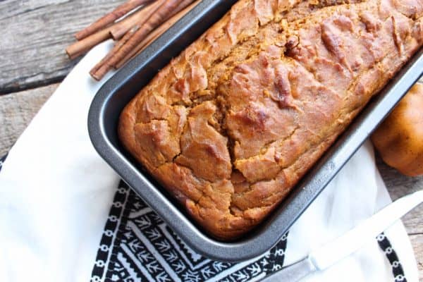 Picture of pumpkin bread in a bread pan with cinnamon sticks. 