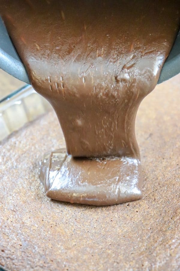 Picture of chocolate fudge icing being poured on brownies.