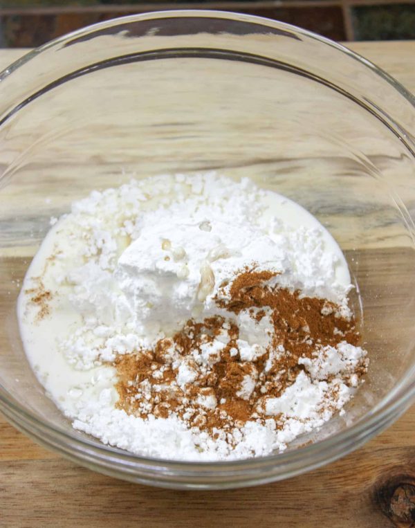 Picture of powdered sugar, vanilla, cinnamon, and cream in a glass bowl.