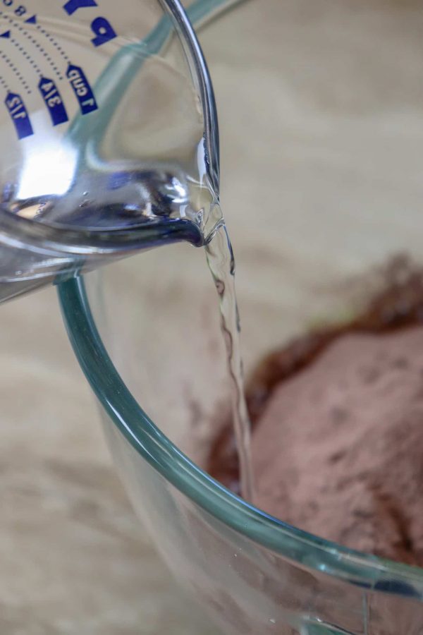 Picture of water being poured into a large glass bowl with instant pudding and chocolate cake mix. 