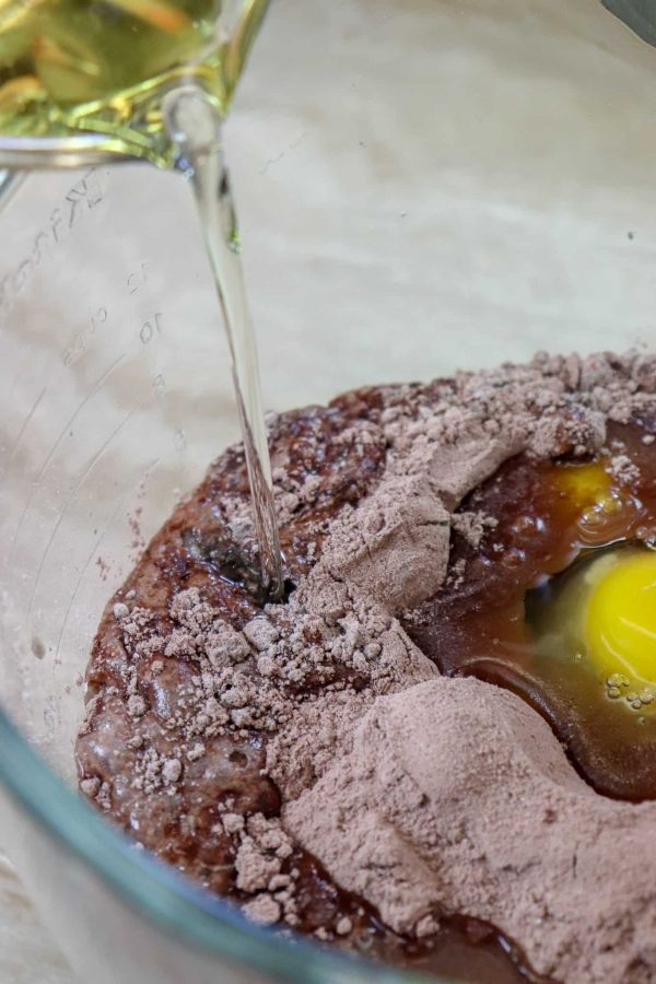 Picture of oil being poured into a glass bowl with cake, eggs, instant pudding, and water. 