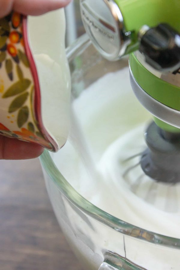 Picture of sugar being poured into a glass bowl with meringue.