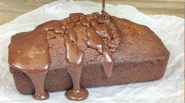 Picture of sweetened condensed milk chocolate pound cake with chocolate frosting being drizzled on the top. 