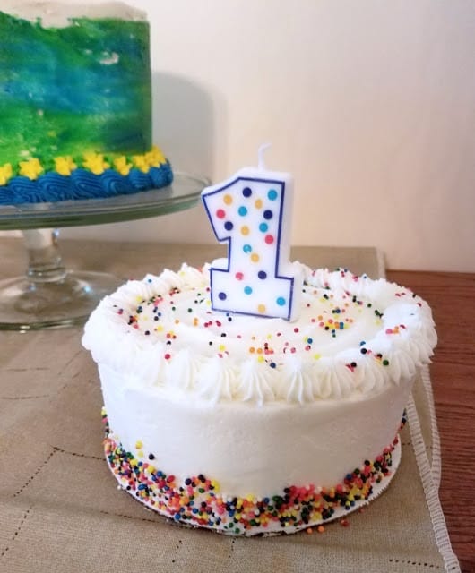 Picture of white birthday cake with green and blue birthday cake in the background.