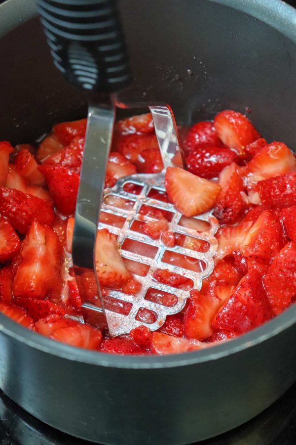 Picture of a potato masher mashing strawberries. 