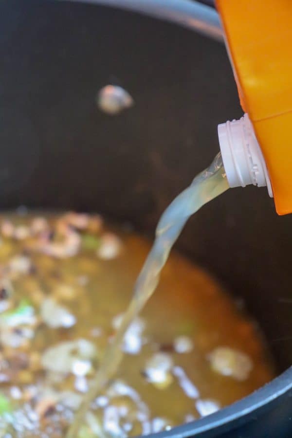 Picture of chicken broth being poured into a saucepan.