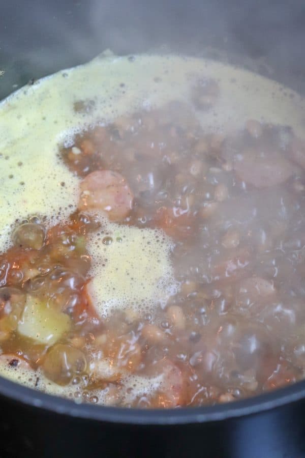 Picture of black eyed pea soup with sausage boiling in a large saucepan