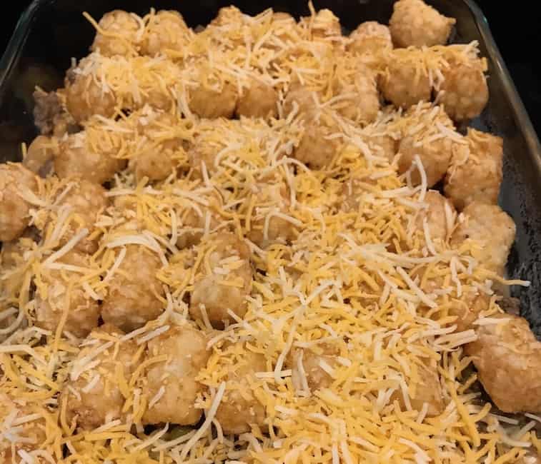 Tater tot casserole with shredded cheese in a large glass dish