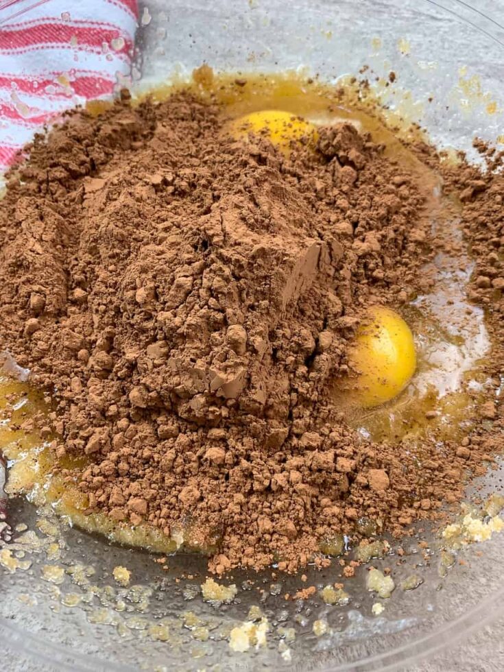 Cocoa powder, with eggs, sugar, and butter in a bowl.