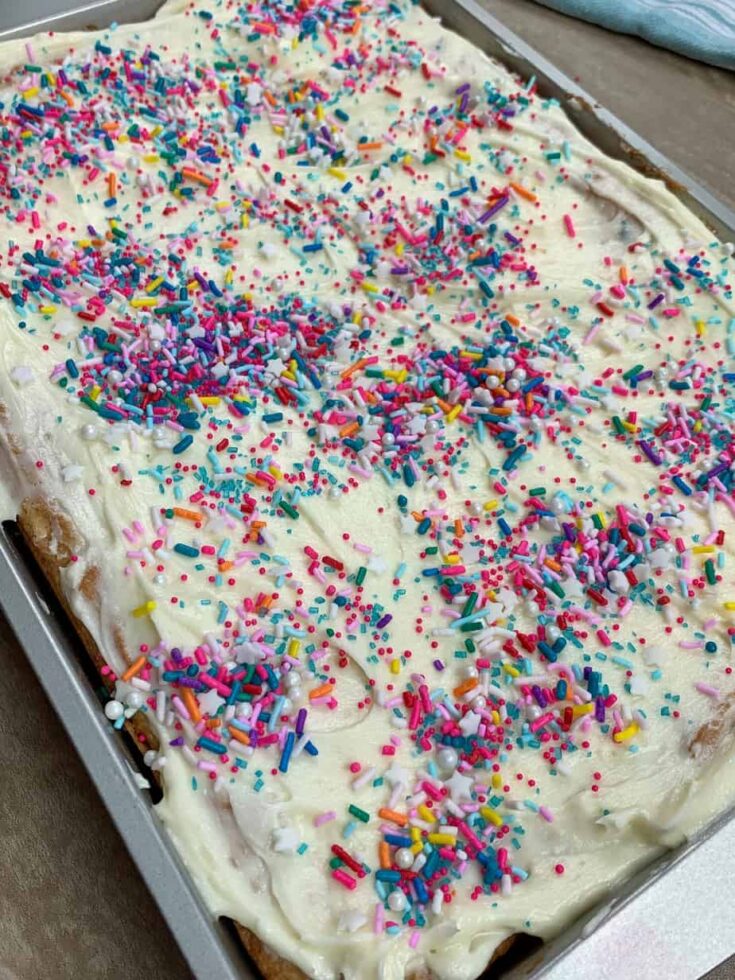 Cookie bars in a cake pan with frosting and sprinkles