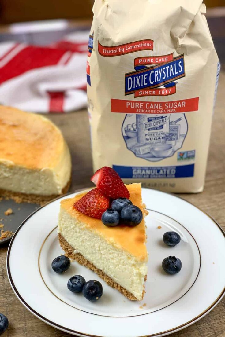 Cheesecake on a plate with a bag of Dixie Crystals sugar. 