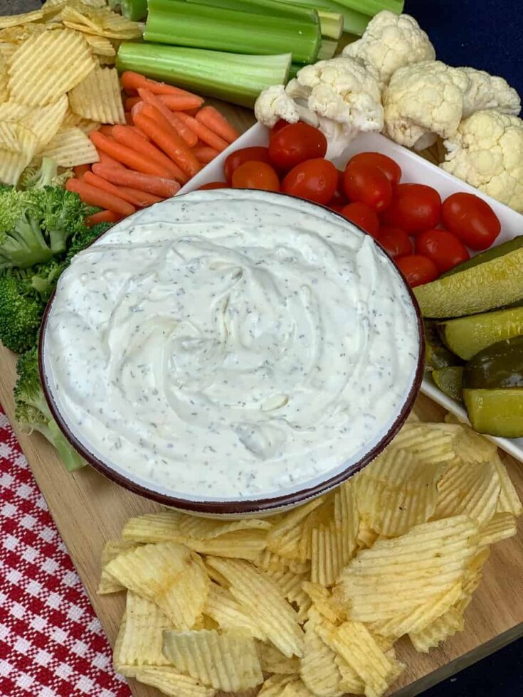 Sour cream dip in a bowl with veggies and chips on a board.