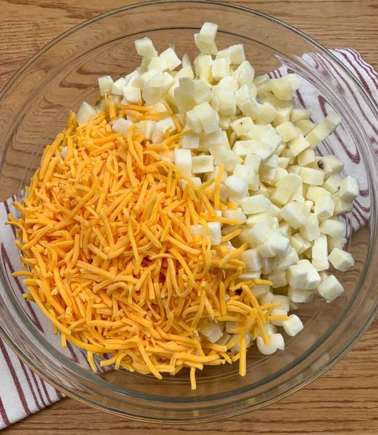 Cubed potatoes and shredded cheddar cheese in a glass bowl