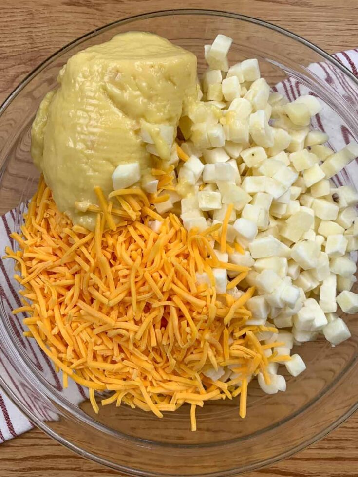 Shredded cheddar cheese, cream of chicken soup, and has brown potatoes in a glass bowl