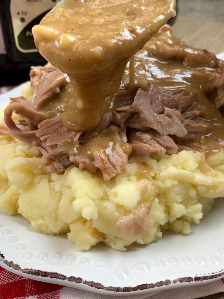 Pouring gravy with a spoon over shredded pork