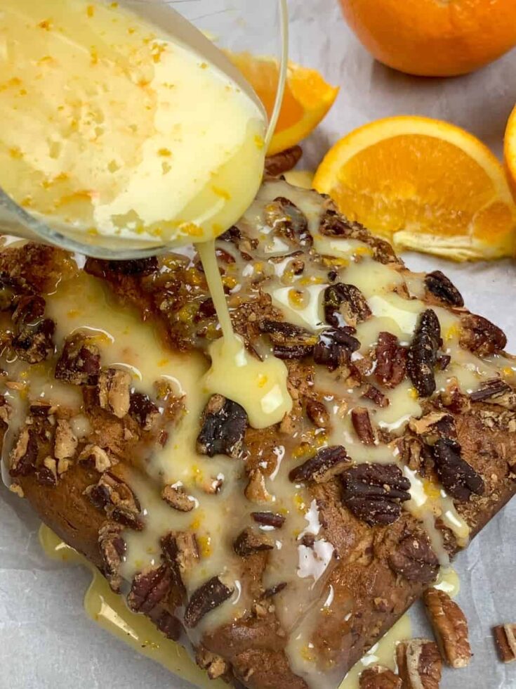 Orange glaze being poured over banana bread with pecans