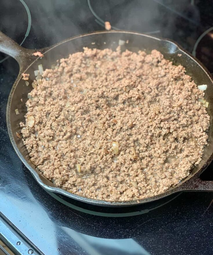 Meat cooking in a cast iron skillet with onions