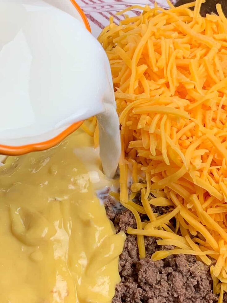 Milk being poured into a bowl with ground beef casserole ingredients.