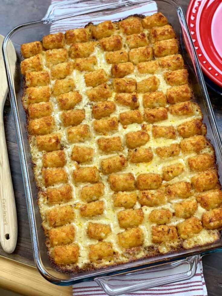 Baked tater tot casserole in a casserole dish next to a red plate