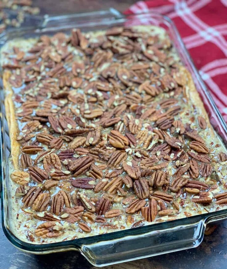 Pecan pie cobbler in a casserole dish with a red towel on the side