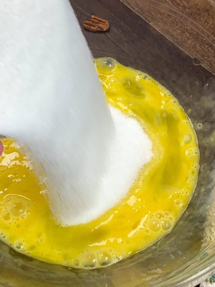 Sugar being poured into a glass bowl with eggs