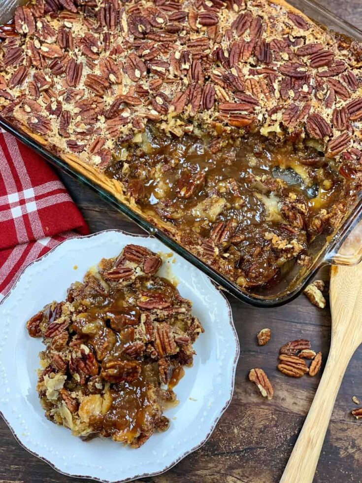 Pecan pie cobbler on a plate with a wooden spoon and casserole dish