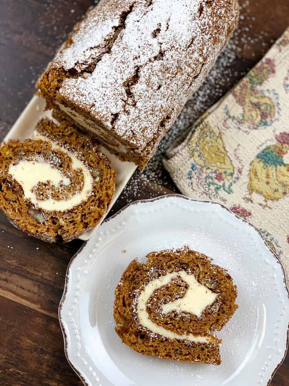 Pumpkin roll log sitting next to a slice of pumpkin roll on a plate