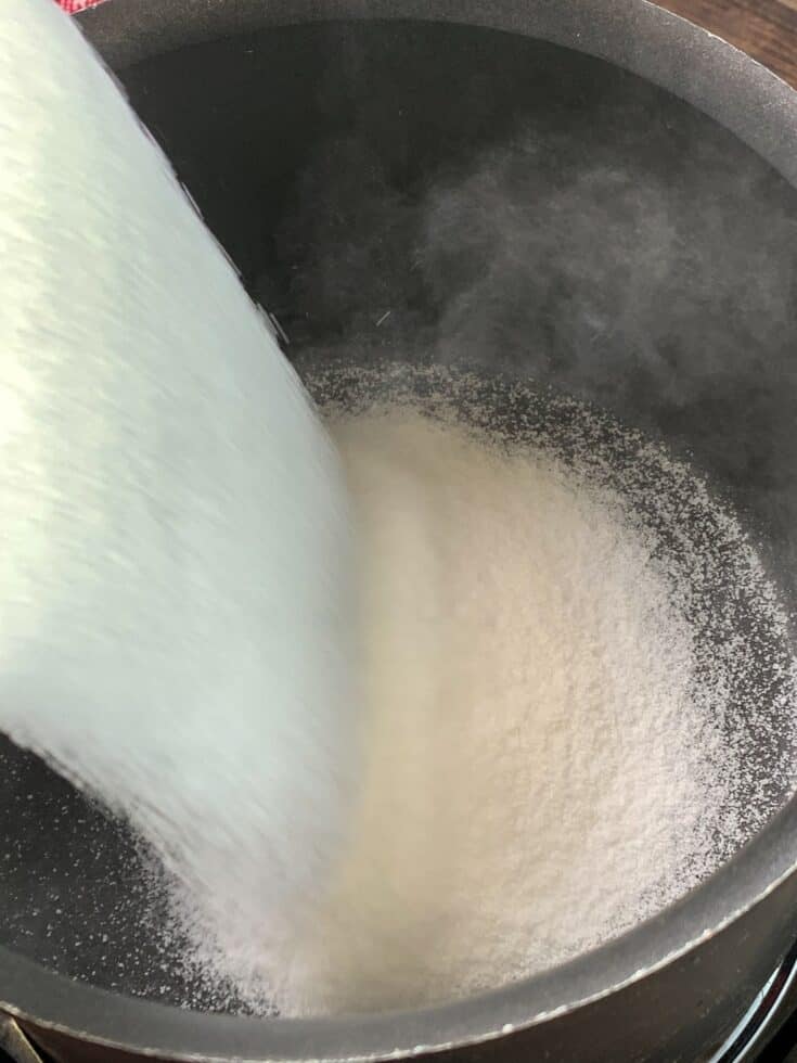 Pouring sugar into a saucepan for candied pecans