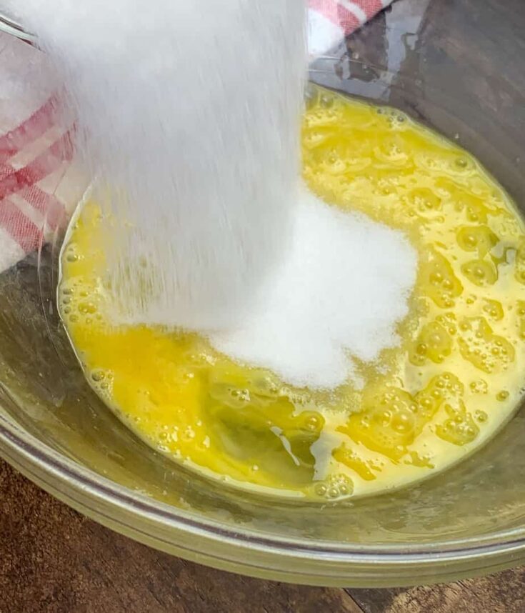 Sugar being poured into a bowl with eggs. 