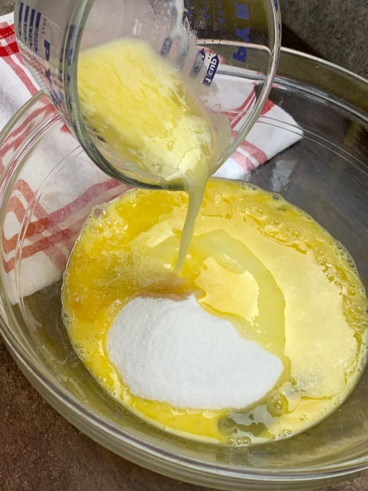 Melted butter being poured into a glass bowl with sugar and eggs