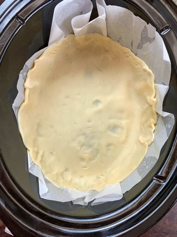 Pie crust spread out in a slow cooker with parchment paper