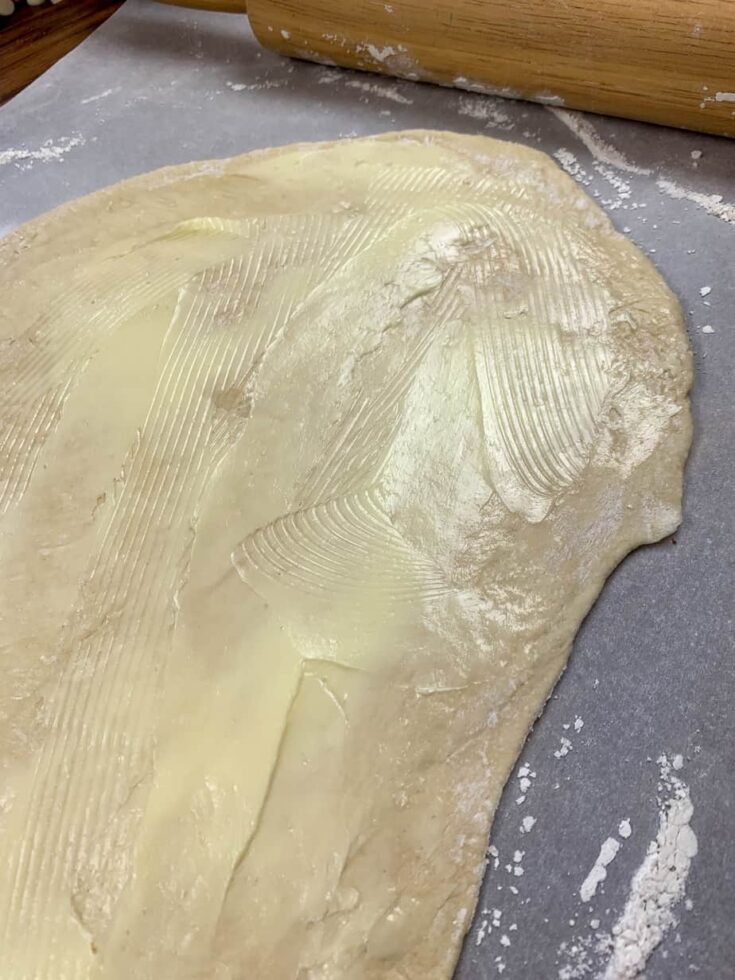 Pizza dough rolled out onto parchment paper with butter spread on top