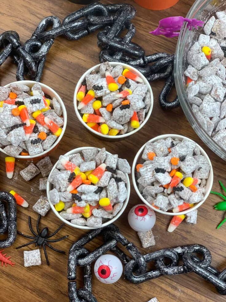 Puppy chow in containers on the counter with candy corn and Halloween candy