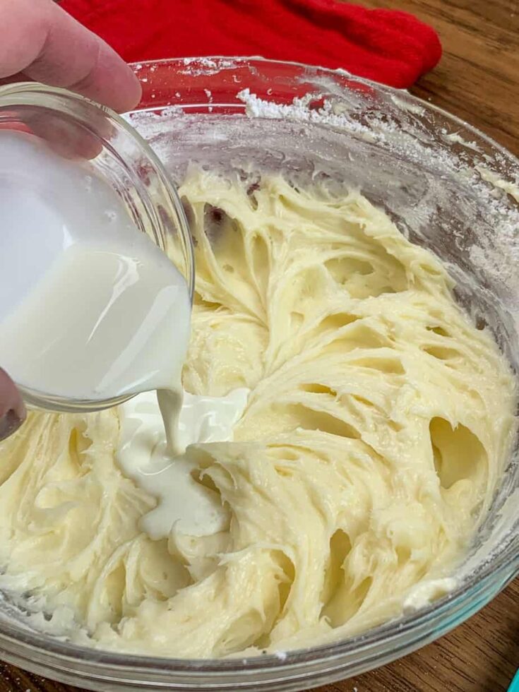 Heavy cream being poured into a bowl of cream cheese frosting for cinnamon rolls. 