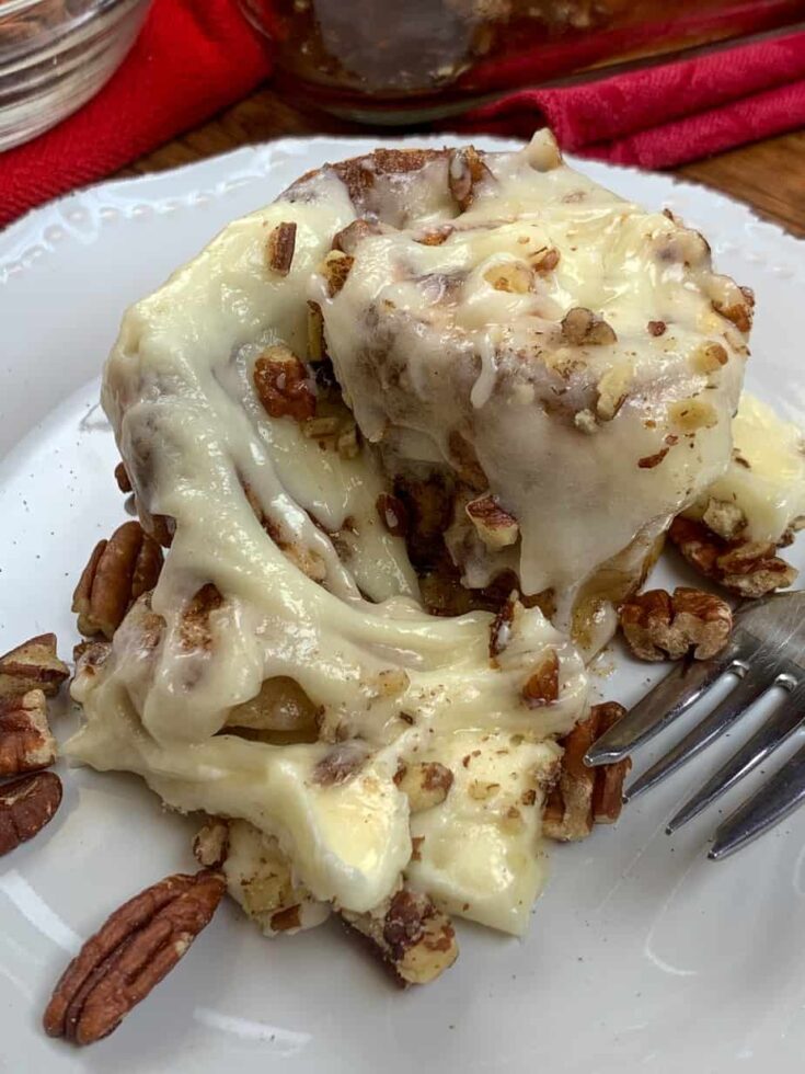 A cinnamon roll with cream cheese icing on top and sprinkled with chopped pecans.