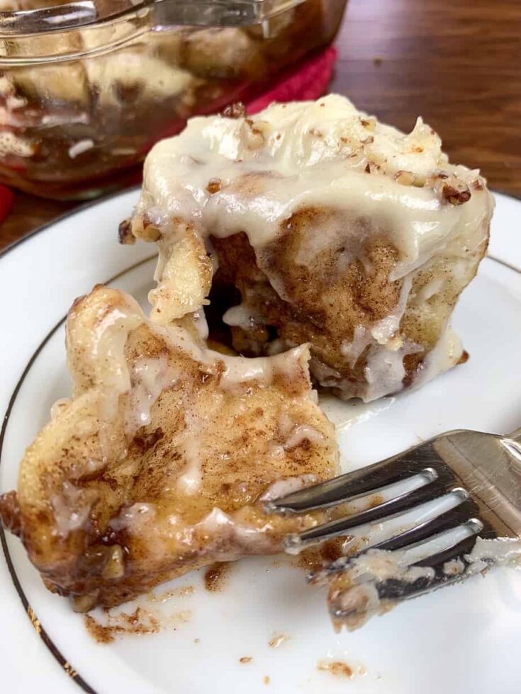 A cinnamon roll on a plate with frosting next to a fork