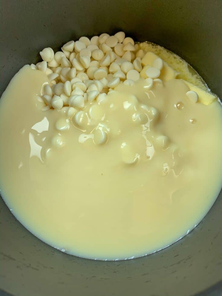 Sweetened condensed milk, white chocolate chips, and butter melting in a saucepan