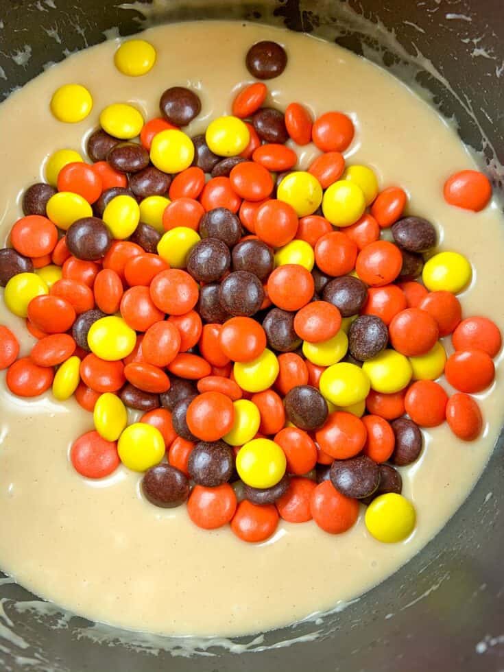 Reese's pieces in a saucepan with melting peanut butter fudge