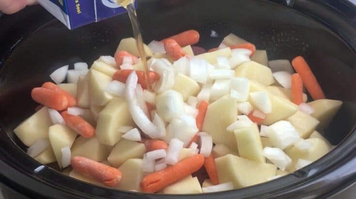 Beef stock being poured over beef stew in a Crock Pot